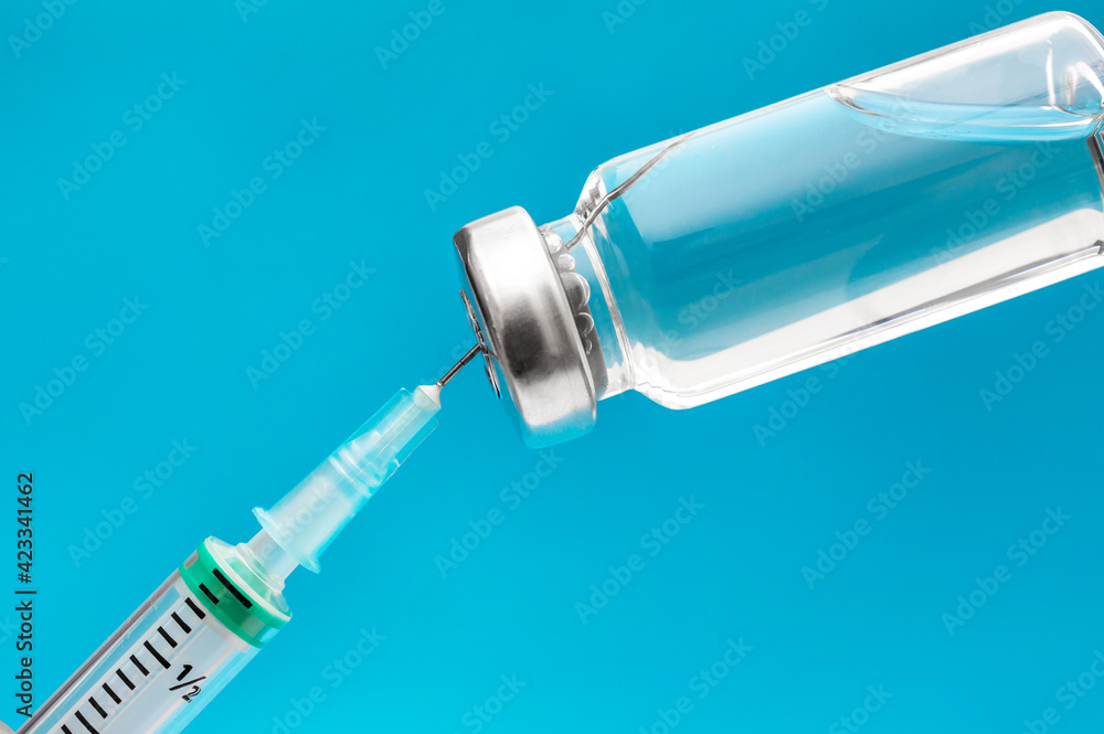 Vaccine vial with medical syringe on blue. Vaccination and immunization. Vaccine vial with medical syringe on blue. Vaccination and immunization.