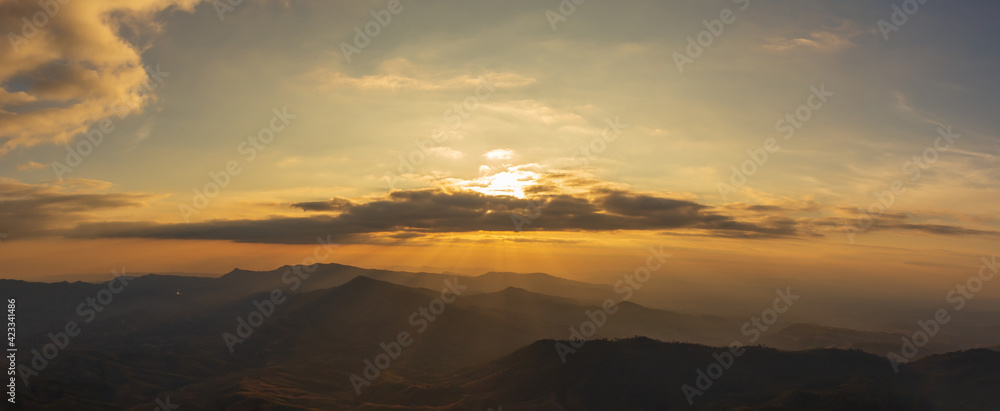 Panorama photo of sunset behind clouds on cliff with mountain hill forest and sunlight sunrays or sunbeams on background.