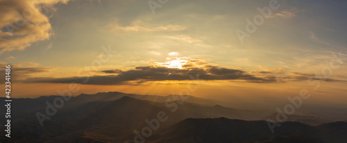 Panorama photo of sunset behind clouds on cliff with mountain hill forest and sunlight sunrays or sunbeams on background.