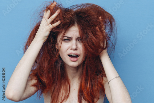 woman touches disheveled hair on her head with her hands on a blue background Copy Space