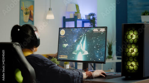 Concentrated woman gamer puting headset starting to play space shooter video game on virtual competition on powerful personal computer. Esport cyber performing during esport gaming tournament