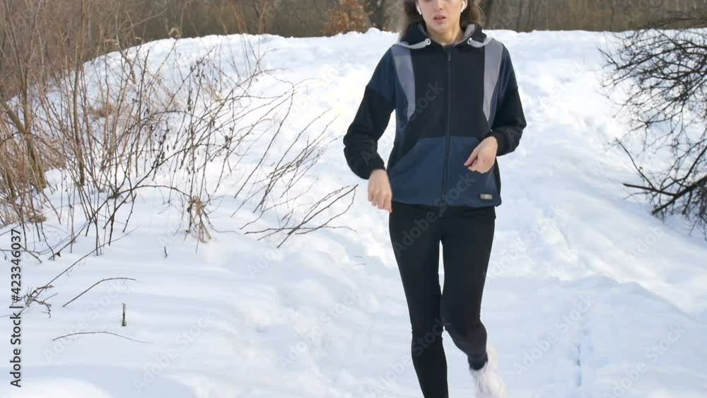 Spring or winter portrait of young athletic girl running in the park in dark sportwear on trees with snow background. Healthy lifestyle concept. Spring or winter portrait of young athletic girl running in the park in dark sportwear on trees with snow background. Healthy lifestyle concept.