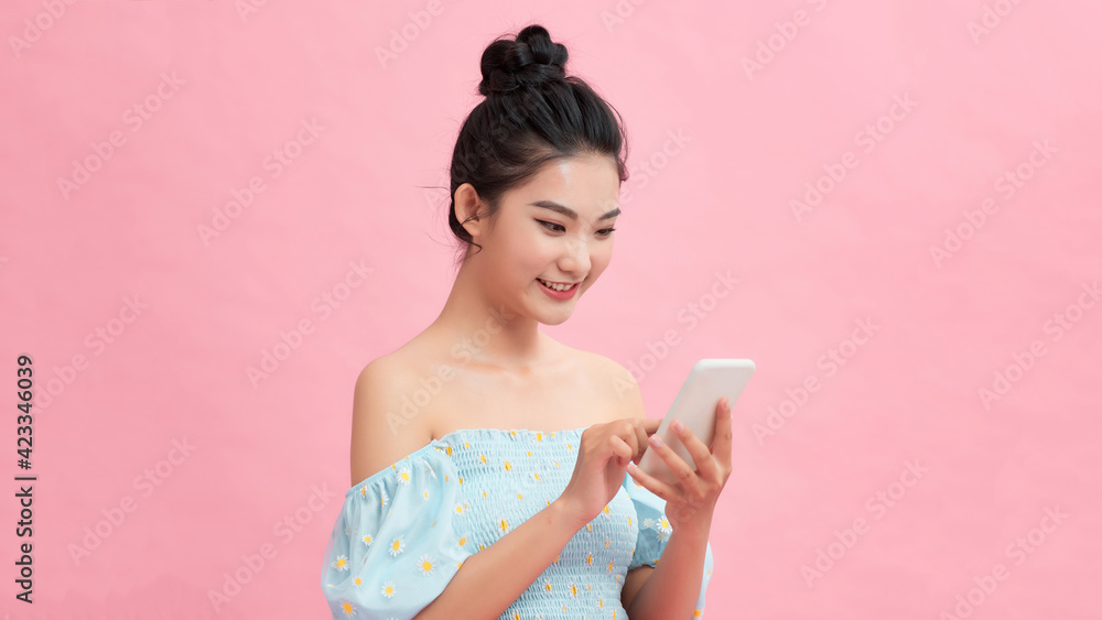 Examining her brand new smart phone. Beautiful young women holding smart phone and smiling while standing against pink background Examining her brand new smart phone. Beautiful young women holding smart phone and smiling while standing against pink background