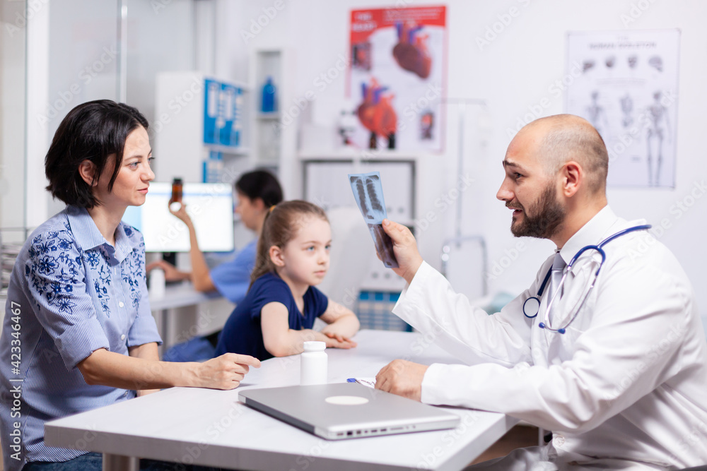 Medical radiologist explaining radiography in hospital office during medical appointment. Pediatrician specialist talking with mother about disease providing professional healdcare treatment Medical radiologist explaining radiography in hospital office during medical appointment. Pediatrician specialist talking with mother about disease providing professional healdcare treatment