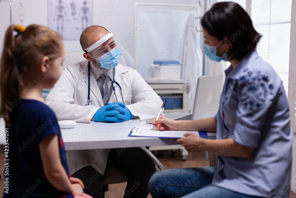 Obraz premium Mother completing medical questionnaire at doctor office in hospital clinic. Pediatrician with protection mask and visor against covid19 talking about diagnostic resultes providing care services