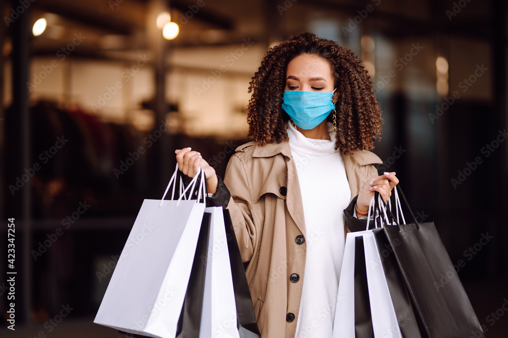 Young woman in protective sterile medical mask on her face with shopping bags after shopping near mall. Spring shopping. Purchases, shopping, lifestyle concept. 