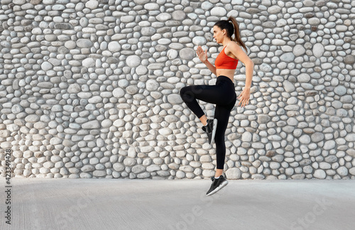 Sports woman dynamic movement jump pose against grey stone wall