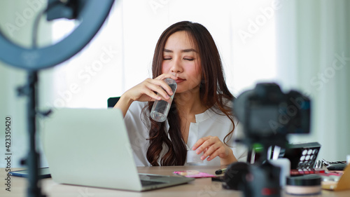 Selective focus on camera, Young and beautiful Asian girl holding a bottle of liquid lotion and smell it showing to camera during broadcast video recording about cosmetics content and review.