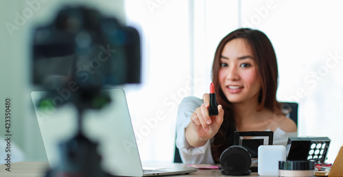 Young and beautiful Asian girl showing lipstick to camera during broadcast or recording video about cosmetics review and beauty blogger. Online selling and marketing concept