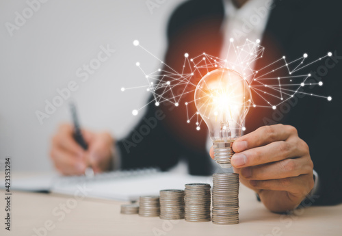 businessman hand holding light bulb with coins stacking on the desk. saving energy and money, the idea with innovation and inspiration concept saving energy and money