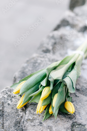A bouquet of yellow tulips lies on a stone surface