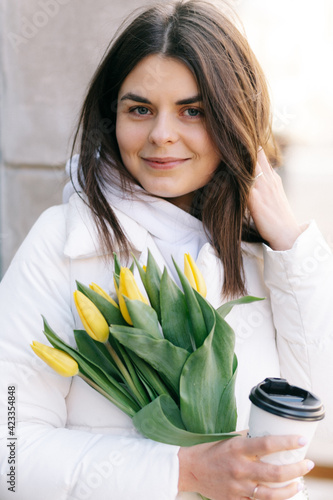 Portrait of a girl with tulips. The girl holds a paper cup with coffee in her hands.