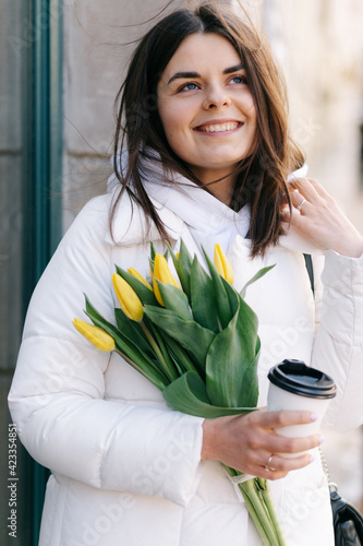 Portrait of a girl with tulips. The girl holds a paper cup with coffee in her hands.