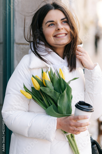 Portrait of a girl with tulips. The girl holds a paper cup with coffee in her hands.