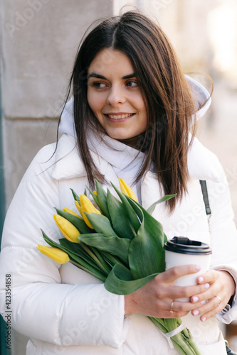 Portrait of a girl with tulips. The girl holds a paper cup with coffee in her hands.
