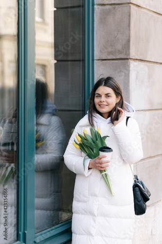 Portrait of a girl with tulips. The girl holds a paper cup with coffee in her hands.