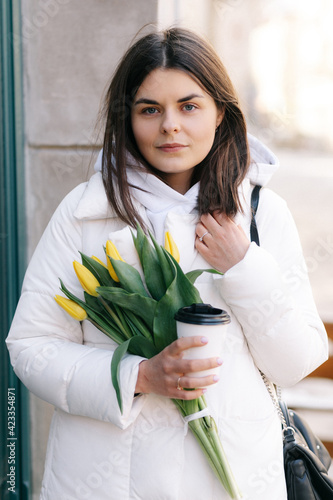 Portrait of a girl with tulips. The girl holds a paper cup with coffee in her hands.