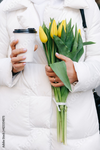 Portrait of a girl with tulips. The girl holds a paper cup with coffee in her hands.