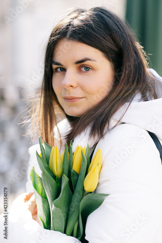 Portrait of a girl with yellow tulips. Girl in a white jacket.