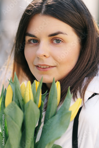 Portrait of a girl with yellow tulips. Girl in a white jacket.