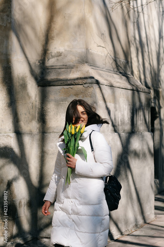 Portrait of a girl with yellow tulips. Girl in a white jacket.
