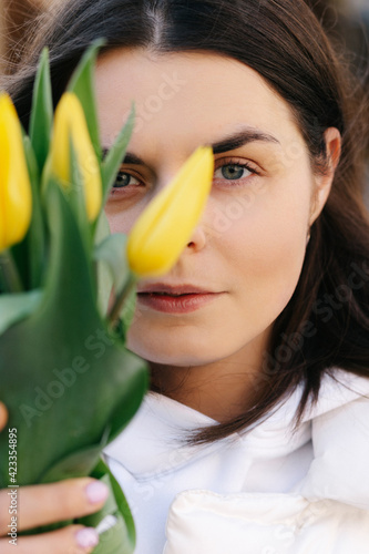 Portrait of a girl with yellow tulips. Girl in a white jacket.