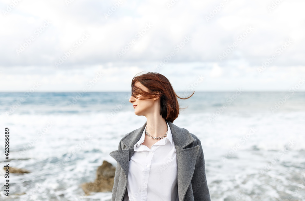 Close-up of a girl with short hair against a cold winter sea. Portrait of a woman on sea with strong wind and rain. wearing grey coat. Freedom and clear mind concept.Human and nature. Mental health Close-up of a girl with short hair against a cold winter sea. Portrait of a woman on sea with strong wind and rain. wearing grey coat. Freedom and clear mind concept.Human and nature. Mental health