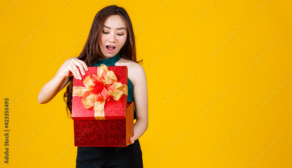Happy smile face cute Asian girl with dark hair holding gift box with delightful and excited, studio shot on yellow background. Celebrate and festival concept. Happy smile face cute Asian girl with dark hair holding gift box with delightful and excited, studio shot on yellow background. Celebrate and festival concept.