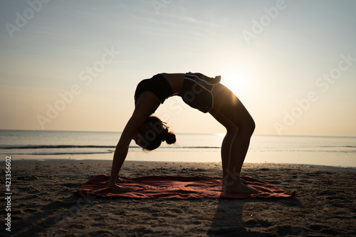Woman training yoga on the beach at sunset in Thailand.