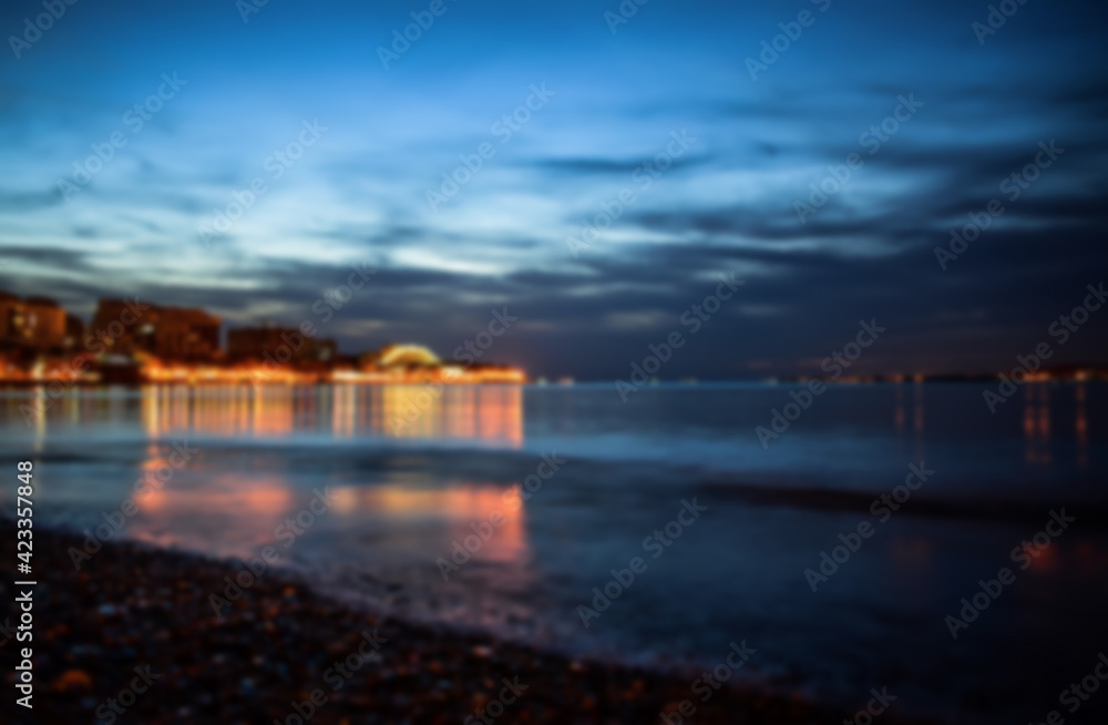 Defocused winter landscape. Cloudy evening view of the bright lights of the buildings and the city center of the resort of Gelendzhik from the sandy beach. Russia, Black sea coast