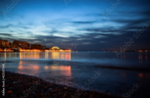 Defocused winter landscape. Cloudy evening view of the bright lights of the buildings and the city center of the resort of Gelendzhik from the sandy beach. Russia  Black sea coast