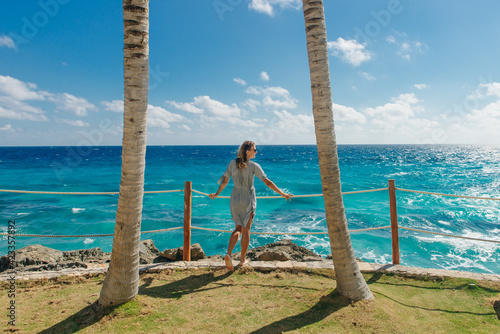 girl stands with her back against the blue ocean between palm trees. Cancun Mexico photo