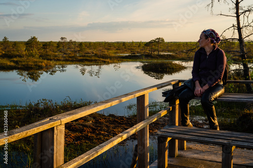 A woman admires the landscape of a forest lake among the raised bogs at sunset. A special observation platform for visitors to the reserve.