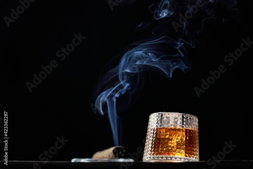 Glass of whiskey and smoking cigar on table. Copy space, black background. Whiskey, brandy, cognac, alcoholic drink .