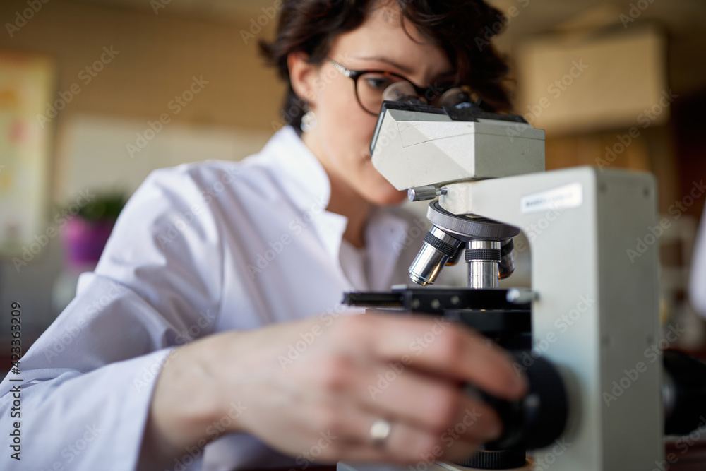 Fototapeta premium A young female scientist looking through the microscope at the university laboratory. Science, chemistry, lab, people