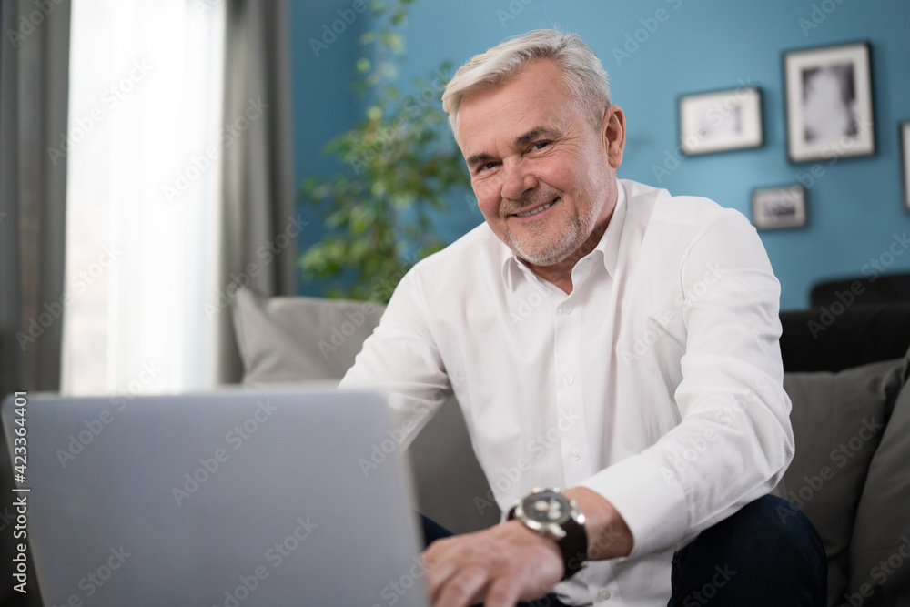 Attractive middle-aged man relaxing at home with his laptop computer looking at the camera with a warm beaming smile Attractive middle-aged man relaxing at home with his laptop computer looking at the camera with a warm beaming smile