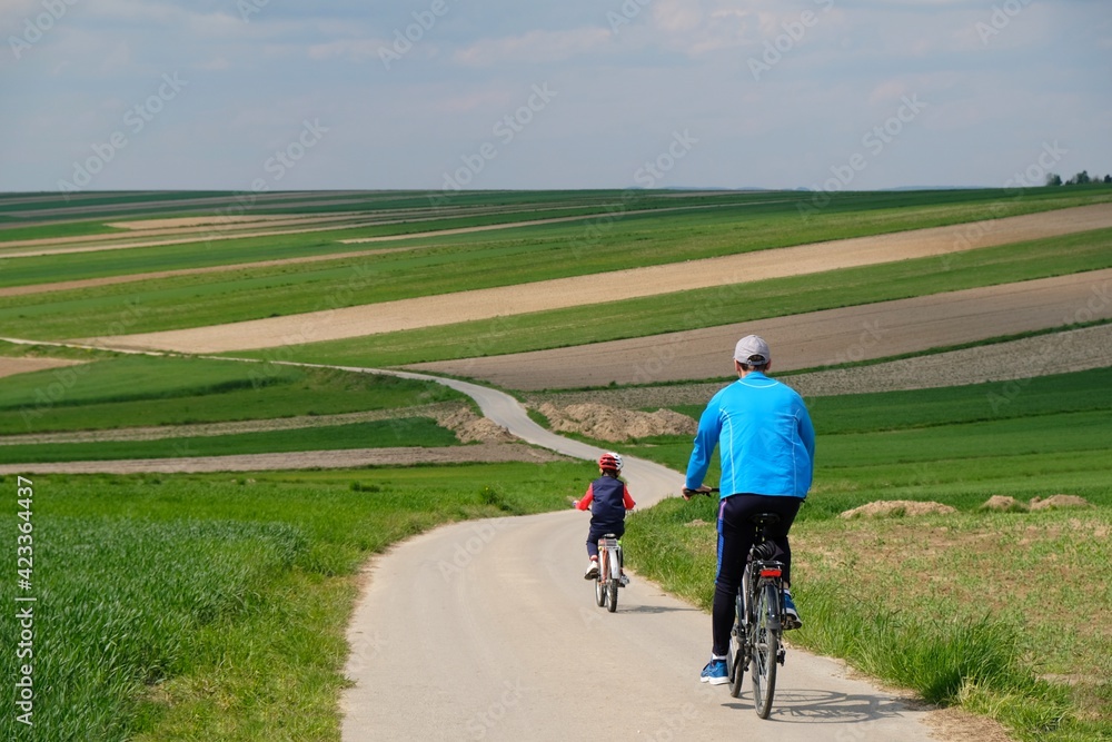 Silhouettes of cyclists on a winding road between beautiful colored fields situated on the hills Silhouettes of cyclists on a winding road between beautiful colored fields situated on the hills