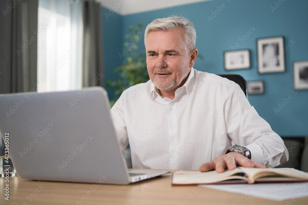Old Senior man checking home finances and bills, he is calculating costs, using computer and writing notes. Elderly Man Reading Documents.
