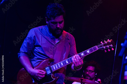 Musician playing electric guitar during rock band live concert. Black hair male guitar player performing on stage. Music lights show