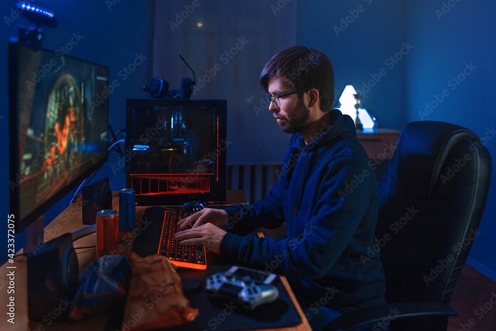 Concentrated Pro Gamer Playing Game, Taking Part In Online Tournament Sitting At Computer At Home. Low Light, Neon Color, Side-View. Professional cybersport player training online game on his PC