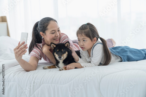 A mom and daughter take a selfie with a Shiba Inu dog on the bed. Japanese dog.