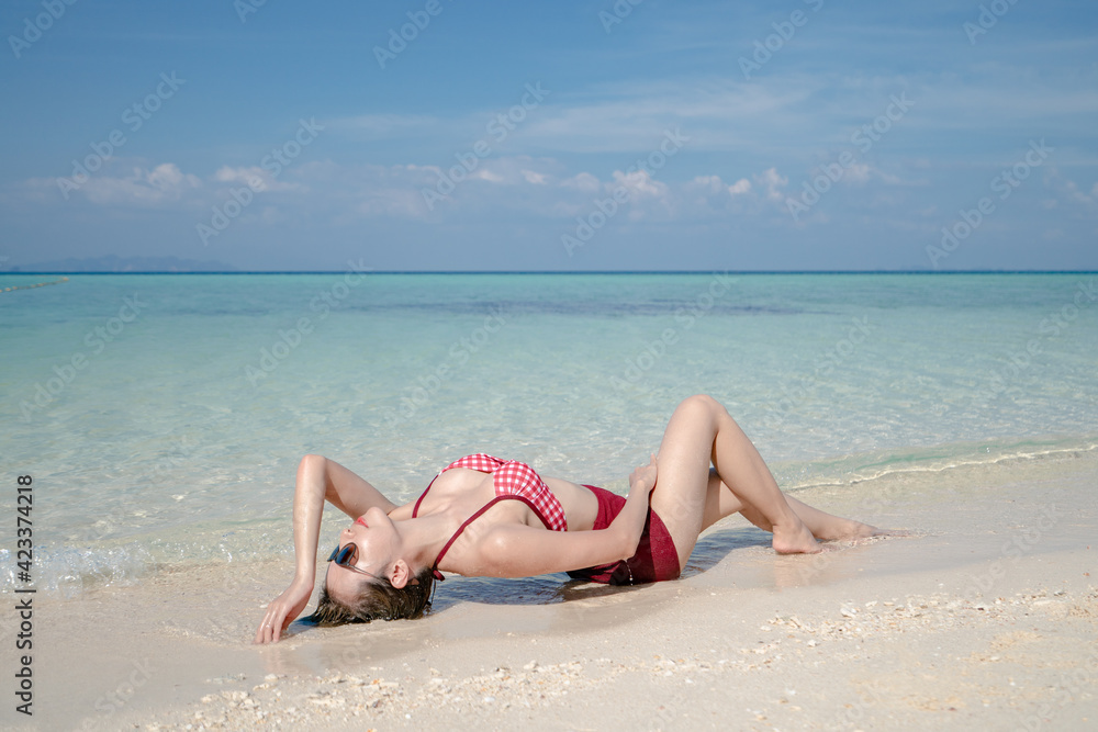 Woman in bikini lying on sea water by white sand beach. Blue sea and sky landscape. summer vacation.