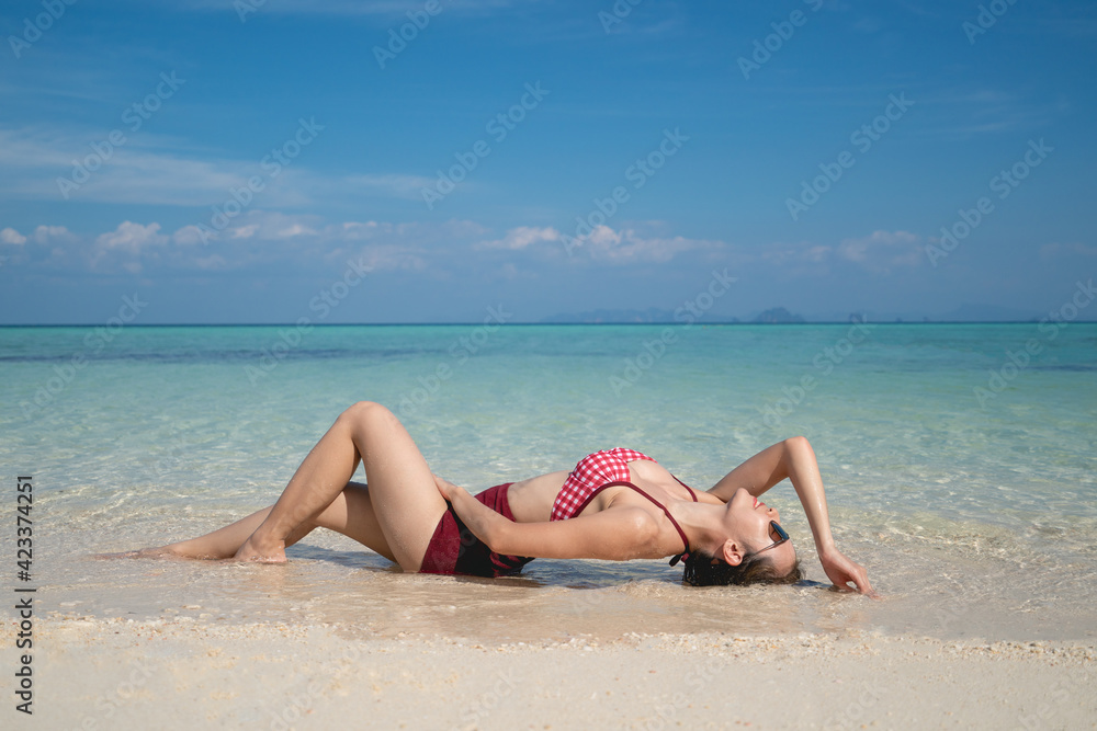 Woman in red bikini swimsuit laying on the sand beach in the clear water. summer vacation. Woman in red bikini swimsuit laying on the sand beach in the clear water. summer vacation.