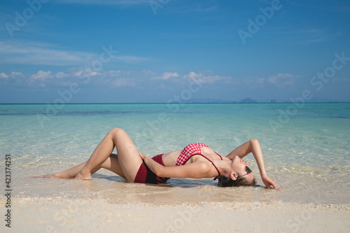 Woman in red bikini swimsuit laying on the sand beach in the clear water. summer vacation.