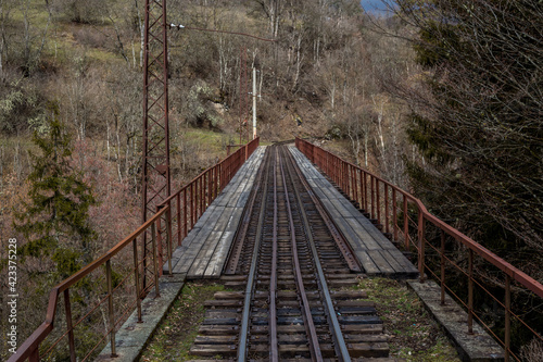 A single-track railway bridge in the woods turns a corner. Spring landscape in the mountains of Georgia.