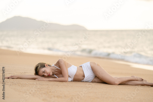 Woman in bikini lying down on sand beach relaxing sunbathing.