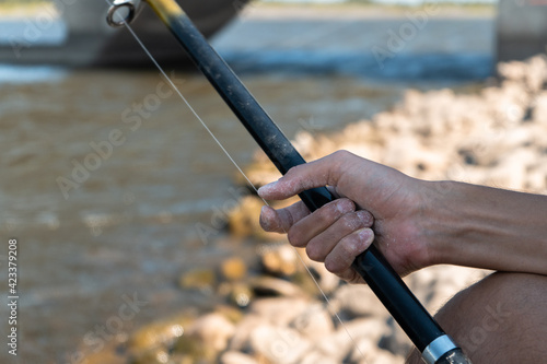 Close-up of an angler's hands holding his fishing rod with a river in the background © Kevin