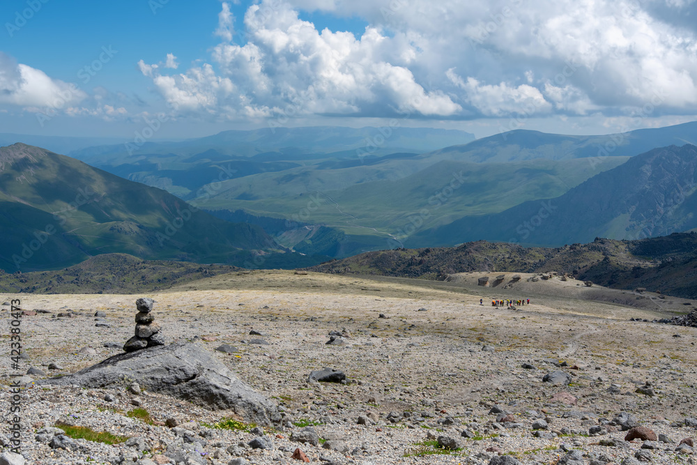 Caucasian landscape. Cairn on Elbrus slope and group of hikers in the distance. Prielbrusye National Park, Kabardino-Balkaria, Caucasus, Russia.