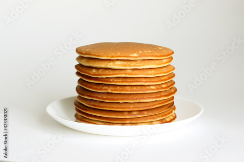 Many pancakes are stacked one on one in a white plate.