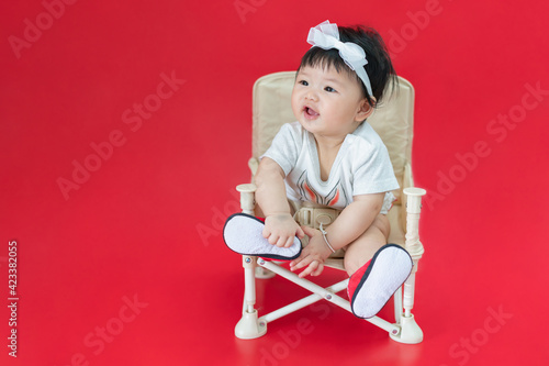 Asian happy baby smiling and sitting on a chair in red color background. Cute 6 months baby with copy space use as concept of bedroom, drypers, development, baby or kid department in hospital. © molpix